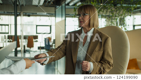 A businesswoman in a modern office handing over a document during a professional meeting or collaboration, highlighting communication and teamwork 124199090