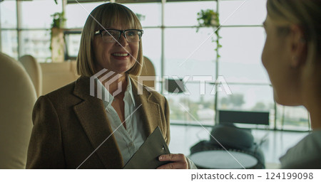 Smiling businesswoman holding a clipboard during a positive discussion in a modern office setting, showcasing confidence, teamwork, and professional interaction 124199098