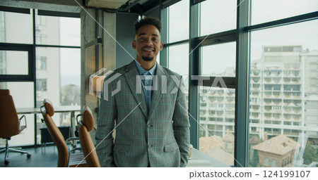 Smiling businessman standing in a modern office with a cityscape view. Smiling businessman standing in a modern office with a cityscape view. 124199107
