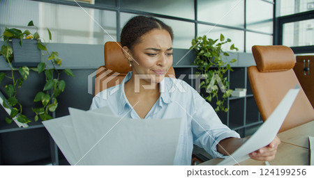 focused young woman analyzing documents at her desk in a modern office, surrounded by charts, a laptop, and office supplies with stylish leather chairs focused young woman analyzing documents at her desk in a modern office, surrounded by charts, a laptop, and office supplies with stylish leather chairs 124199256