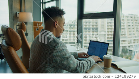 A businessman working on a laptop in a modern office with large windows and a cityscape view, showcasing focus and productivity. A businessman working on a laptop in a modern office with large windows and a cityscape view, showcasing focus and productivity. 124199279