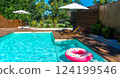 Modern backyard swimming pool with turquoise water, wooden deck, umbrellas, lounge chairs, and pink donut inflatable 124199546
