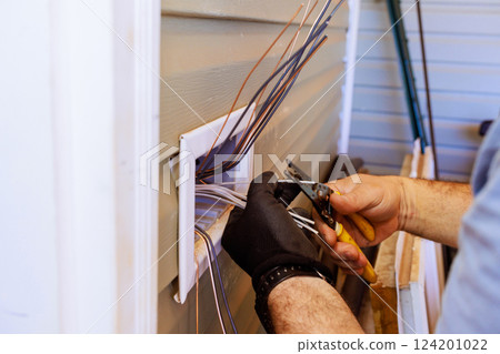 An electrician carefully strips wires while installing electrical connections during home renovation working 124201022