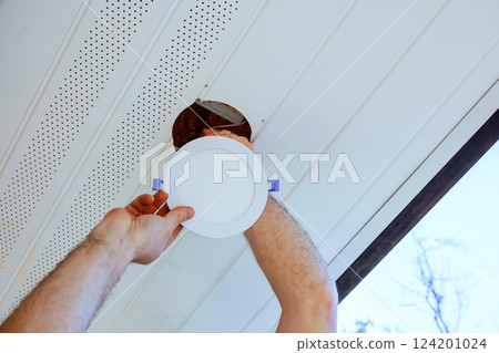 Worker mounting ceiling led light fixture while installing it in bright, contemporary soffit natural light. 124201024