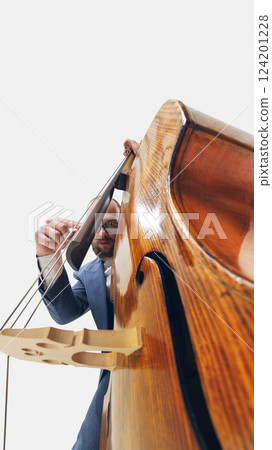 Extreme low-angle view of male musician in glasses playing double bass, deeply connected to instrument on white background. 124201228