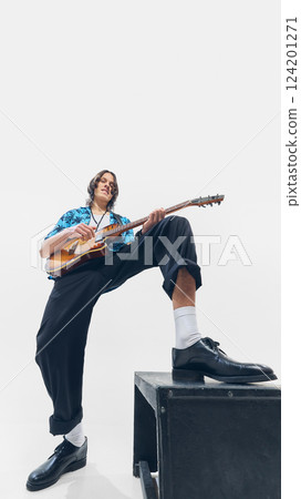 Low-angle image of energetic young man, confidently playing electric guitar, standing on elevated surface on white background. Low-angle image of energetic young man, confidently playing electric guitar, standing on elevated surface on white background. 124201271