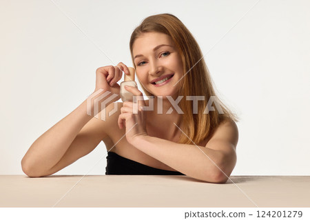 Hydration and nourishment. Woman sitting with skincare product in hands, smiling confidently against white background 124201279