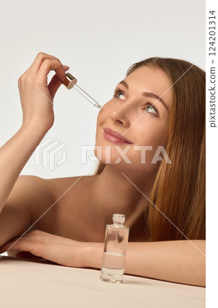 Elegant young woman with smooth, glowing, clear skin, applying moisturizing rejuvenating facial serum against white background Elegant young woman with smooth, glowing, clear skin, applying moisturizing rejuvenating facial serum against white background 124201314