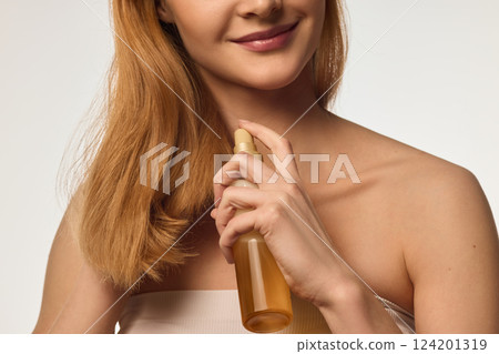 Cropped image of woman taking care after her hair, applying moisturizing and protective hair spray against white background Cropped image of woman taking care after her hair, applying moisturizing and protective hair spray against white background 124201319