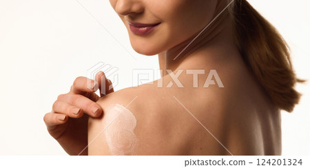 Cropped image of young woman applying body lotion on shoulder, promoting skin hydration and softness. 124201324