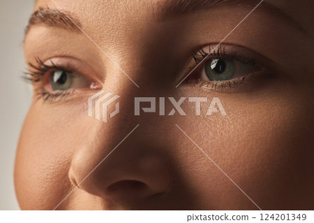 Close-up of female face, green eyes, well-defined lashes, smooth complexion, soft lighting enhancing natural beauty. 124201349