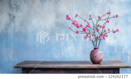 A wooden table holds a vase with pink flowers 124202177
