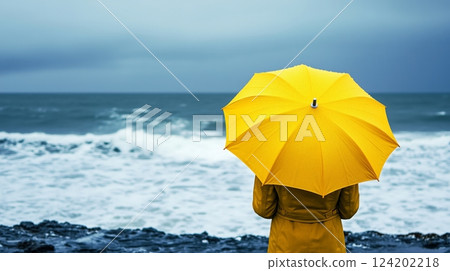Bright yellow umbrella against stormy ocean backdrop 124202218