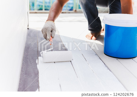 Worker painting decking floor in white color with a roller. 124202676