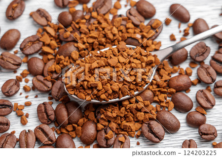 Soluble granules in metal spoon with scattered roasted Arabica coffee beans on aged white wooden surface. Mixed ingredients of instant and brewed beverage. Top View Soluble granules in metal spoon with scattered roasted Arabica coffee beans on aged white wooden surface. Mixed ingredients of instant and brewed beverage. Top View 124203225