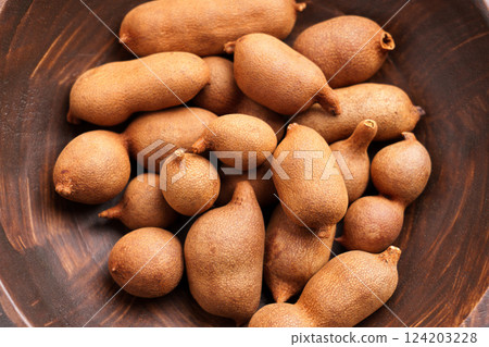 Fresh tamarind fruits in rustic wooden bowl. Sweet exotic tropical snack. Whole pods. Tamarindus indica. Top view 124203228