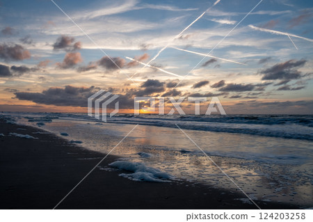 A stunning sunset over the ocean with cloud trails and gentle waves creates a picturesque scene 124203258