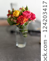 A bouquet of decorative roses stands on the table in a transparent glass. 124203417