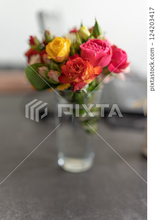 A bouquet of decorative roses stands on the table in a transparent glass. 124203417