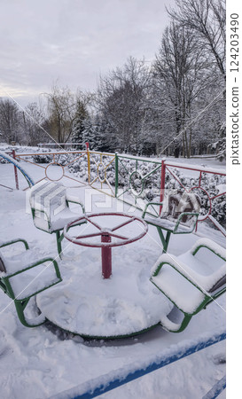 Children's playground covered with snow. Empty swings and slides. 124203490