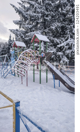 Children's playground covered with snow. Empty swings and slides. Children's playground covered with snow. Empty swings and slides. 124203491