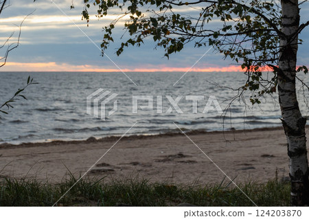 Peaceful scene of a sandy beach at sunset with vibrant hues in the sky. 124203870