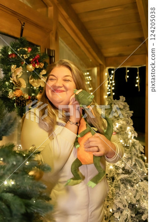 Woman Christmas Tree Toy Smiling - A woman is standing in front of a Christmas tree, smiling and holding a stuffed toy. Woman Christmas Tree Toy Smiling - A woman is standing in front of a Christmas tree, smiling and holding a stuffed toy. 124205038