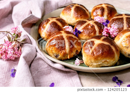 Traditional hot cross buns on ceramic plate decorated with edible flowers. Easter homemade pastry arranged on light texture background with linen napkin and violet petals. Traditional hot cross buns on ceramic plate decorated with edible flowers. Easter homemade pastry arranged on light texture background with linen napkin and violet petals. 124205123
