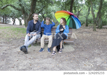 Family sitting on bench with rainbow umbrella in park 124205233