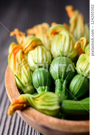 Close up of young zucchini with flowers in wooden bowl Close up of young zucchini with flowers in wooden bowl 124205502