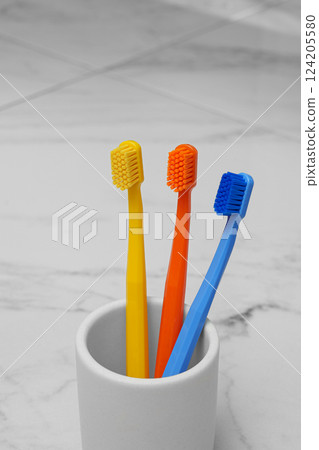 Three colored brushes in a glass in the bathroom. Light photo. Oral hygiene. 124205580