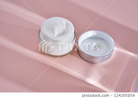 An open jar of cream with its texture on a pink background. An open jar of cream with its texture on a pink background. 124205859
