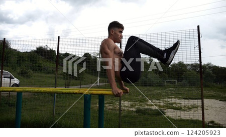 Strong guy training abdominal muscles on parallel bars at sports ground. Young shirtless sportsman exercising at nature. Sporty athlete working out at nature. Concept of active sportive lifestyle 124205923