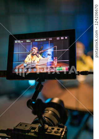 Cheerful young man recording podcast in studio. Confident man with headphones and microphone recording a podcast. Happy guy talking on web radio. 124206670