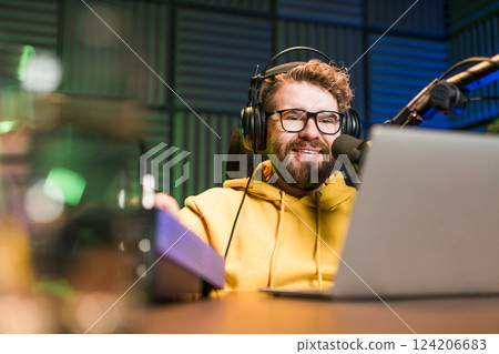 Young smiling male radio presenter talking into the microphone and reading news, information and communication concept. Podcast and internet streaming concept. Young smiling male radio presenter talking into the microphone and reading news, information and communication concept. Podcast and internet streaming concept. 124206683