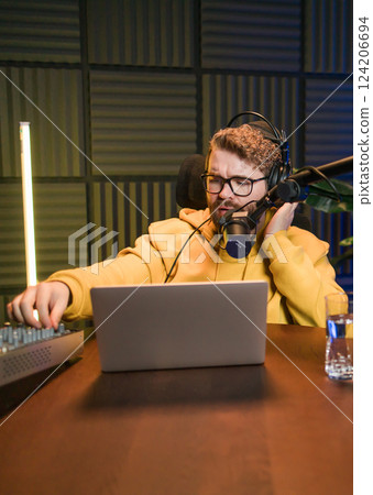 Cheerful young man recording podcast in studio. Confident man with headphones and microphone recording a podcast. Happy guy talking on web radio. 124206694
