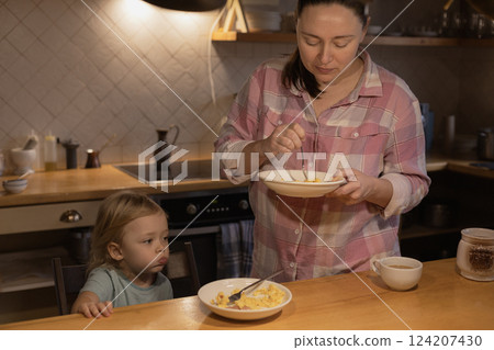 A woman is eating in the kitchen next to a child who is having breakfast 124207430
