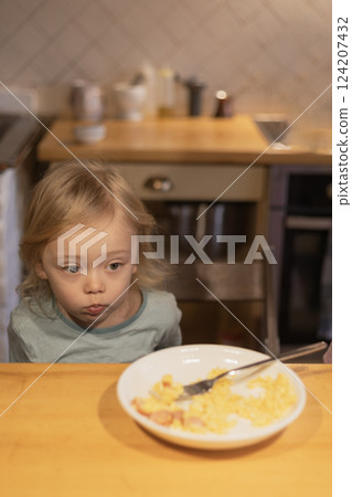 Three-year-old child sitting at the table next to a plate of food, breakfast 124207432