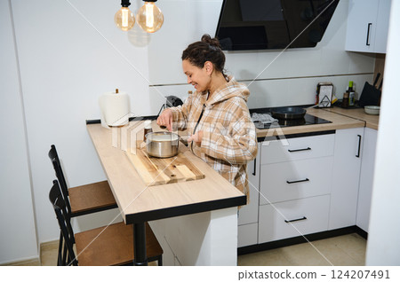 Smiling Woman Preparing a Meal in a Modern Home Kitchen Setting Smiling Woman Preparing a Meal in a Modern Home Kitchen Setting 124207491
