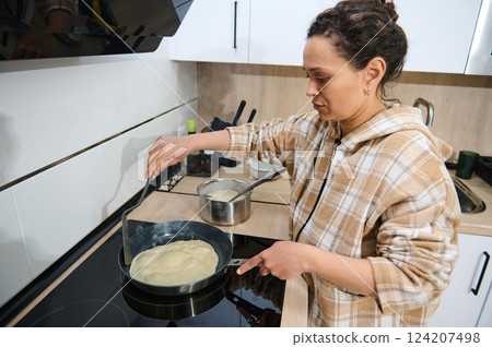 Woman Cooking Crepes on a Stove in a Bright Modern Kitchen Woman Cooking Crepes on a Stove in a Bright Modern Kitchen 124207498