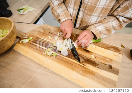 Person Slicing Vegetables on a Wooden Cutting Board in Modern Kitchen Person Slicing Vegetables on a Wooden Cutting Board in Modern Kitchen 124207550