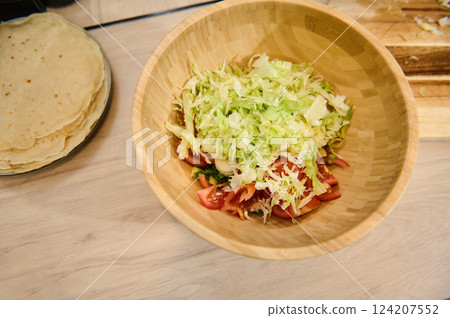 Fresh Salad in Wooden Bowl Next to Homemade Tortillas on Kitchen Table Fresh Salad in Wooden Bowl Next to Homemade Tortillas on Kitchen Table 124207552