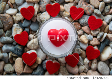 Romantic candle and red bright fabric hearts on other stones near the river. Romantic candle and red bright fabric hearts on other stones near the river. 124207680