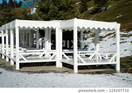 White canopies stand gracefully against a snowy backdrop in a serene mountain setting, inviting visitors to enjoy the beautiful winter landscape under a clear blue sky 124207710