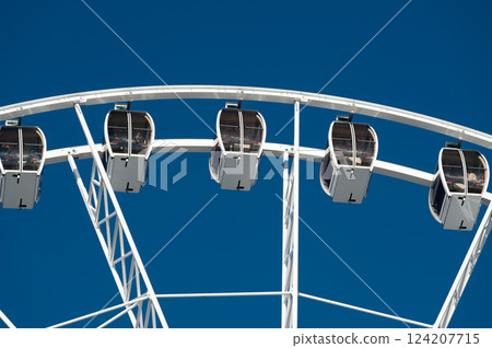 Bright blue sky over a towering ferris wheel showcasing colorful cabins in a lively amusement park on a sunny afternoon adventure filled with laughter 124207715