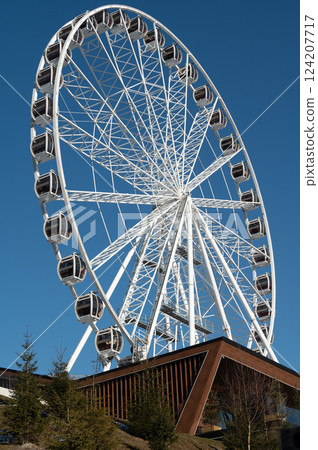 Majestic ferris wheel towering against a vibrant blue sky, inviting thrill-seekers to enjoy breathtaking views and unforgettable experiences 124207717