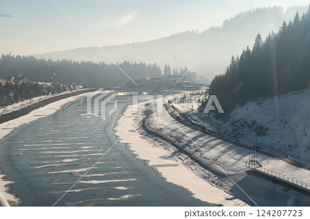 Majestic winter landscape of a frozen river snaking through pine forests and distant hills under a clear blue sky 124207723