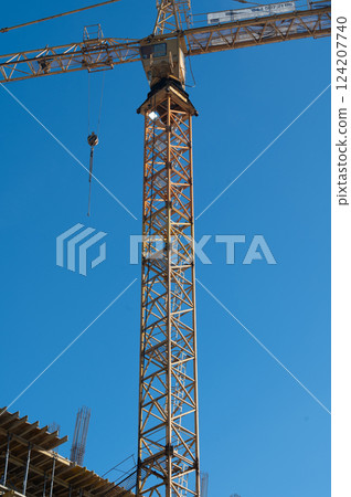 Construction crane reaches new heights against a clear blue sky with a bustling construction site below, symbolizing progress and development in urban settings 124207740