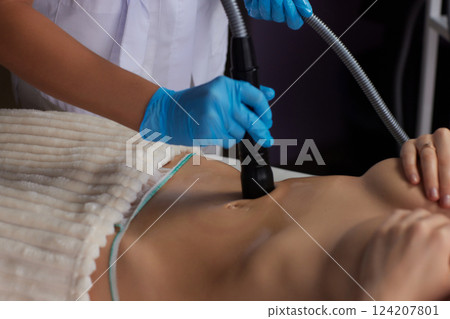 procedure removing cellulite on female abdomen, cavitation belly massage. Ultrasonic massage for weight loss. Correction of female figure without surgical intervention. Closeup of the tummy procedure removing cellulite on female abdomen, cavitation belly massage. Ultrasonic massage for weight loss. Correction of female figure without surgical intervention. Closeup of the tummy 124207801