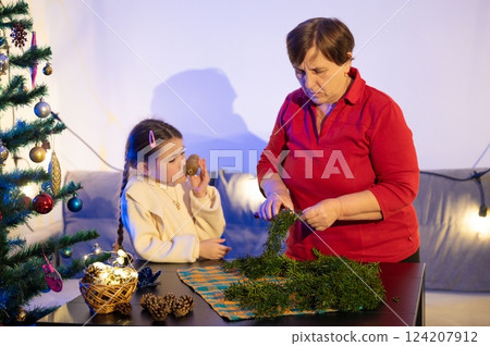 Grandmother and granddaughter prepare festive greenery for the holidays, creating a charming winter scene. 124207912